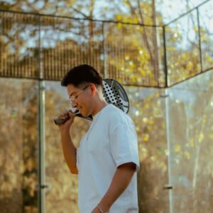 Young man holding a padel racket at an outdoor court on a sunny autumn day.