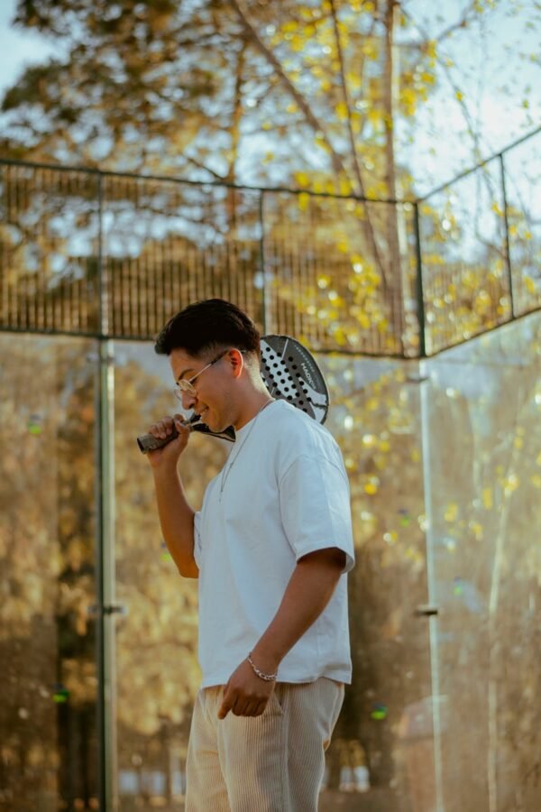 Young man holding a padel racket at an outdoor court on a sunny autumn day.